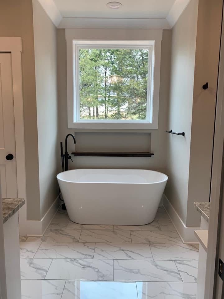 a white bath tub sitting under a window next to a sink in a room with marble flooring