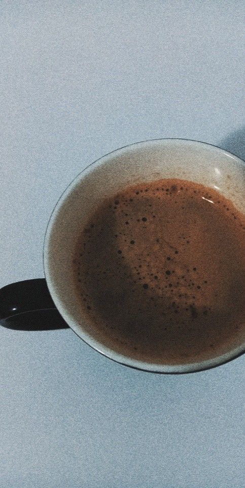 a cup of coffee sitting on top of a white table next to a black spoon