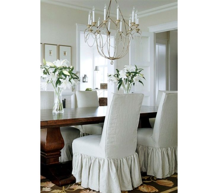 a chandelier hangs above a dining room table with white chairs and flowers in vases