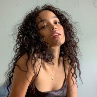 a woman with long curly hair sitting on top of a bed next to a white wall