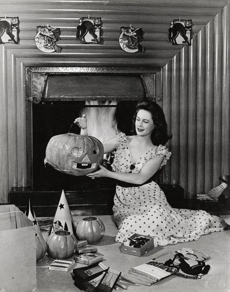 a woman sitting on the floor next to a fire place holding a pumpkin in her hand