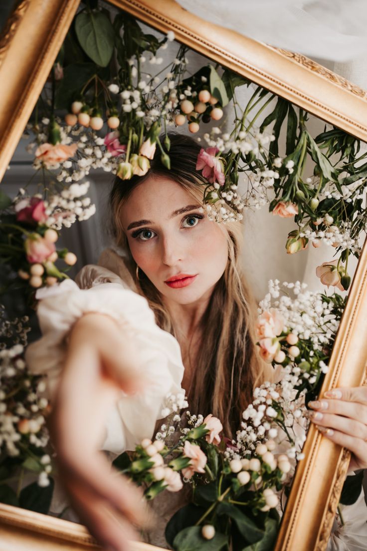 a woman is holding flowers in front of her face and looking at the camera through a mirror