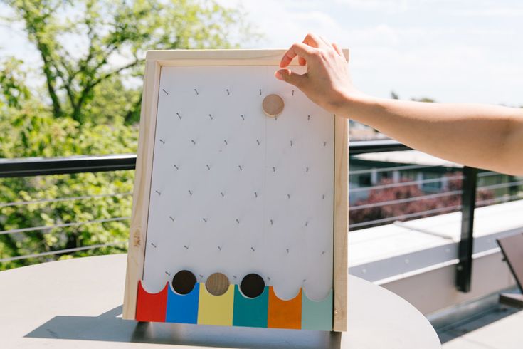 a person holding up a board with holes in it on top of a table next to a railing