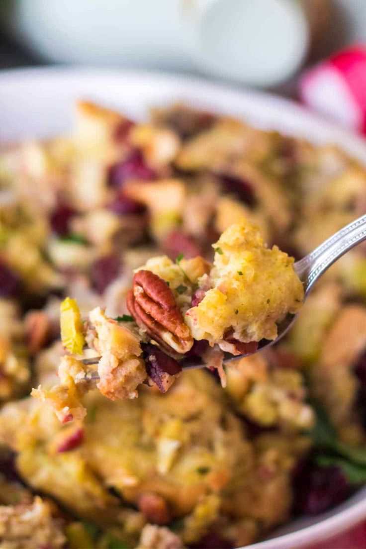 a close up of a spoonful of stuffing in a bowl with cranberries