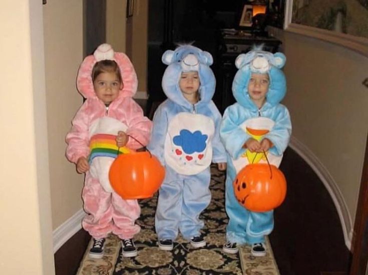 three children dressed up in costumes standing on a carpeted hallway with balloons and pumpkins