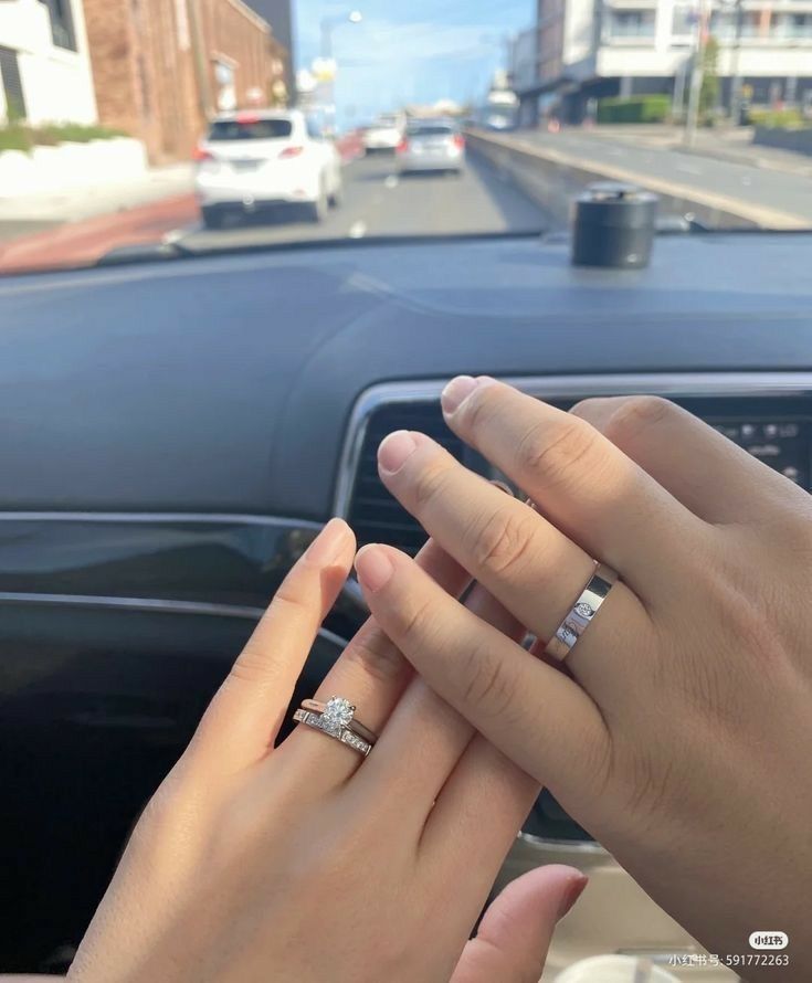 two people holding hands in front of a car on a street with buildings and cars behind them