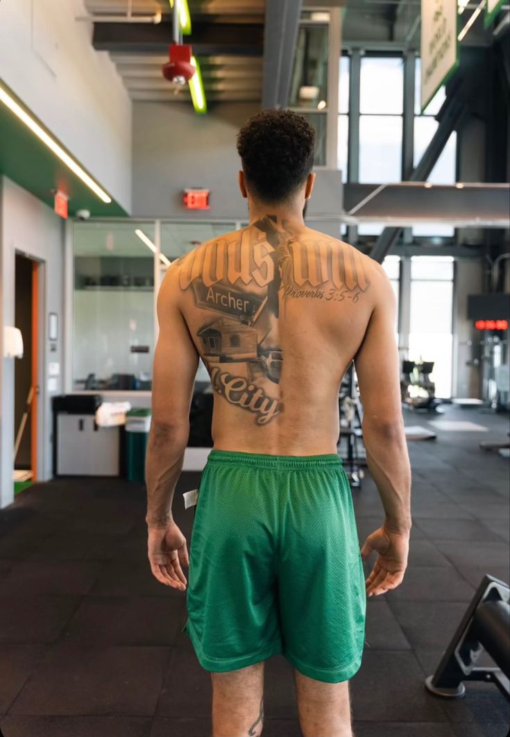 a man with tattoos on his back standing in a gym