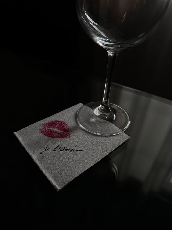 a wine glass sitting on top of a table next to a napkin with a lipstick imprint