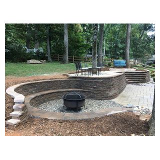 an outdoor fire pit surrounded by stone steps and landscaping area with trees in the background