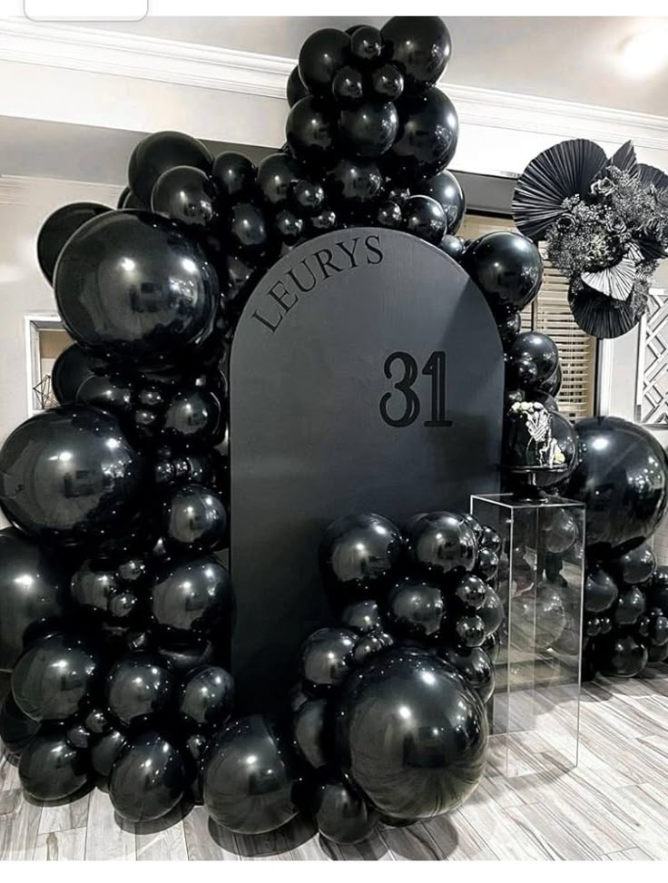 black balloons are arranged in the shape of an arch with a plaque on one side