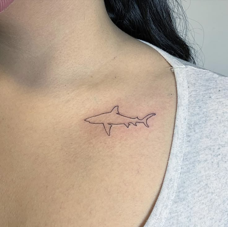 a woman's chest with a small tattoo of a shark on the left side