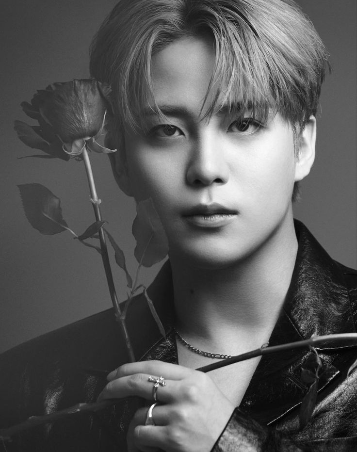 a young man holding a rose in his right hand and looking at the camera with an intense look on his face