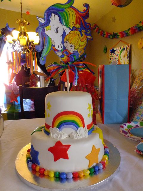 a birthday cake decorated with rainbows and stars on a table in a children's room