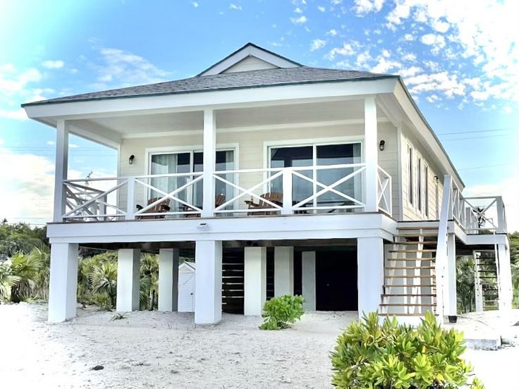 a white house on the beach with stairs leading up to it's second floor