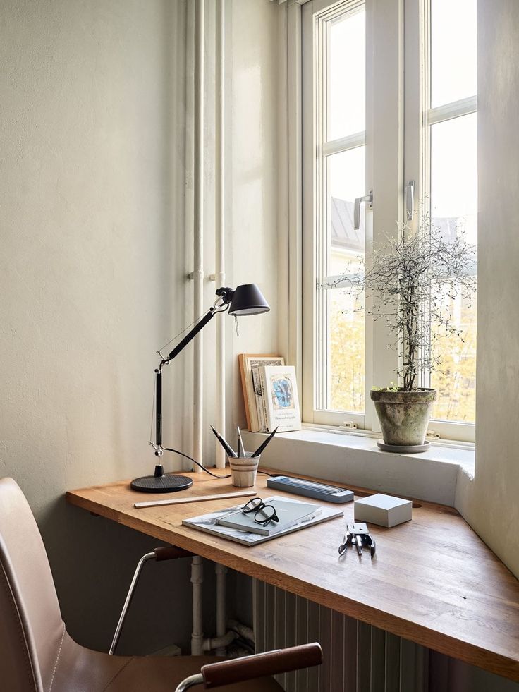 a wooden desk with a lamp and pictures on it next to a window in a room