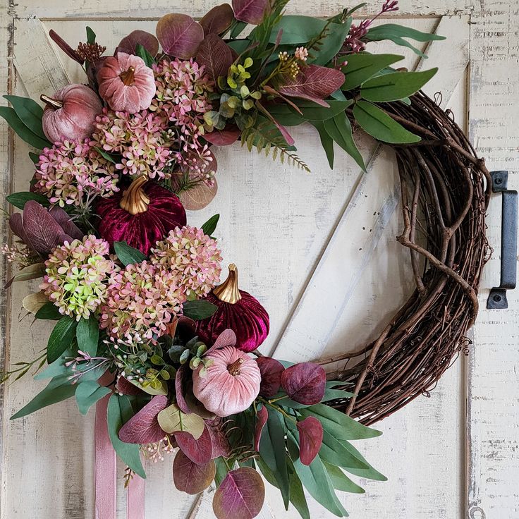 a wreath with pink flowers and greenery hanging on a door