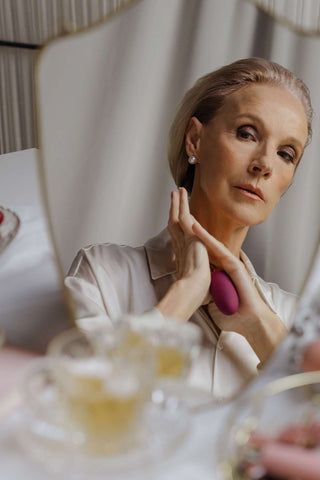 a woman sitting at a table with her hand on her chin and looking in the mirror