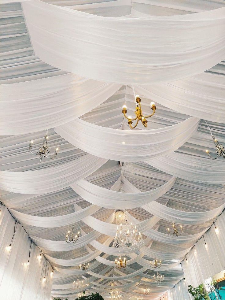 the ceiling is decorated with white drapes and chandeliers for an elegant wedding