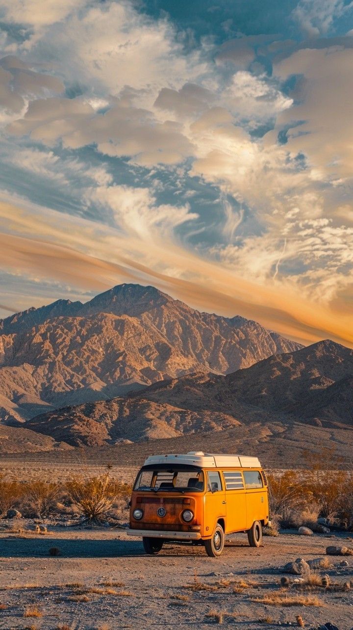 an orange and white van parked in the desert with mountains in the background at sunset