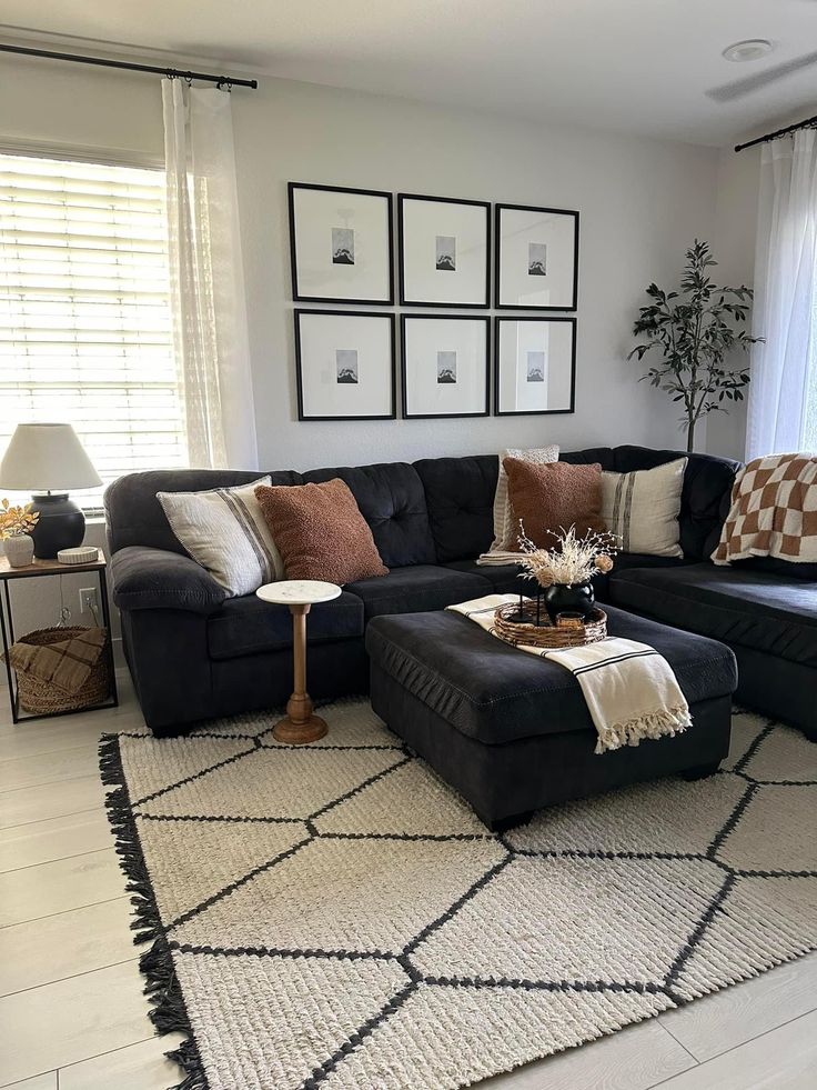 a living room with black couches and pillows on the rug in front of windows