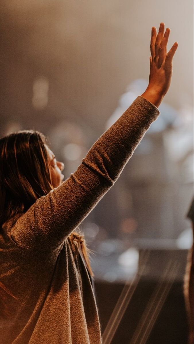 a woman with her hands up in the air at a music festival or concert, she is wearing a brown sweater