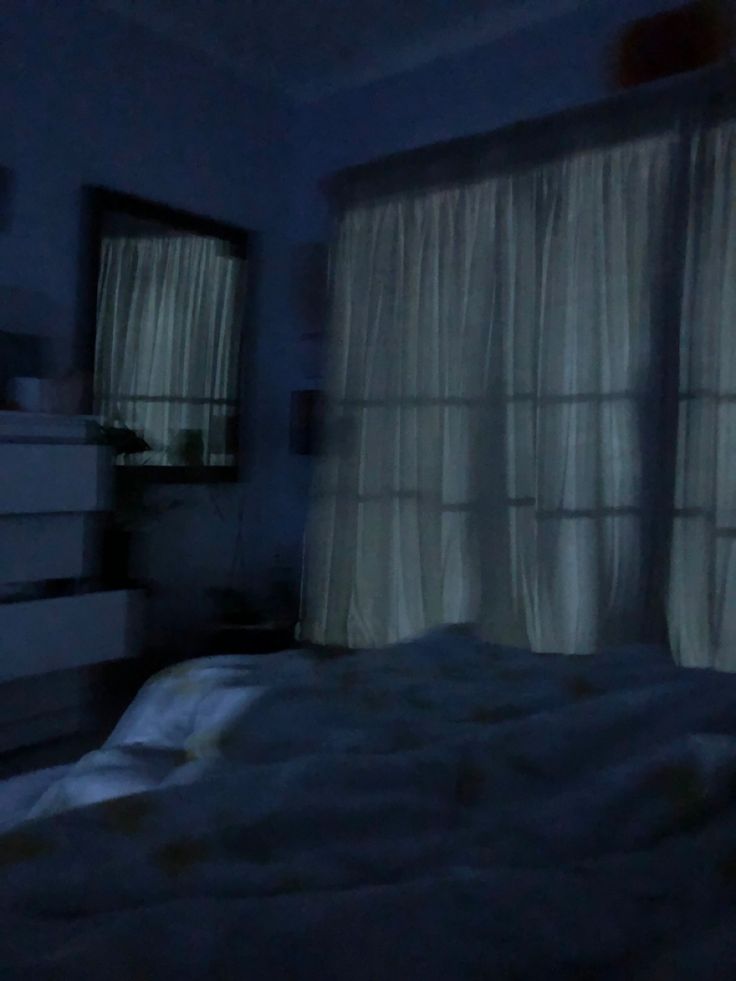 a blurry image of a bed in a dark room with curtains on the windows