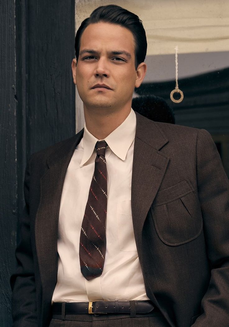 a man wearing a suit and tie standing in front of a door with his hands in his pockets