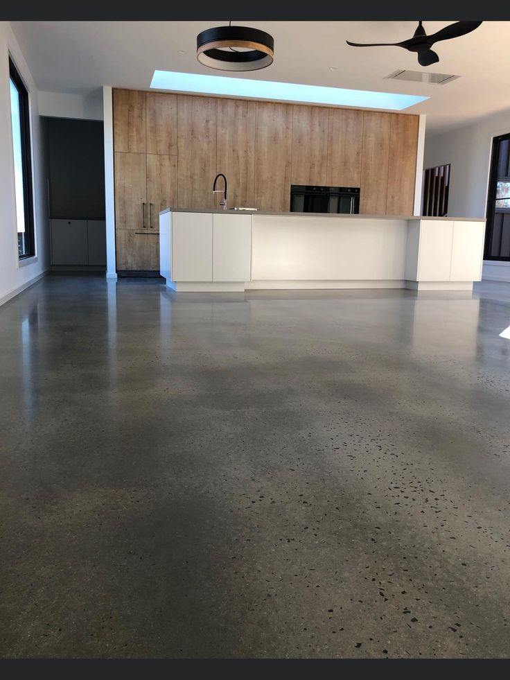 an empty living room with concrete flooring and ceiling fan in the center, next to a kitchen island