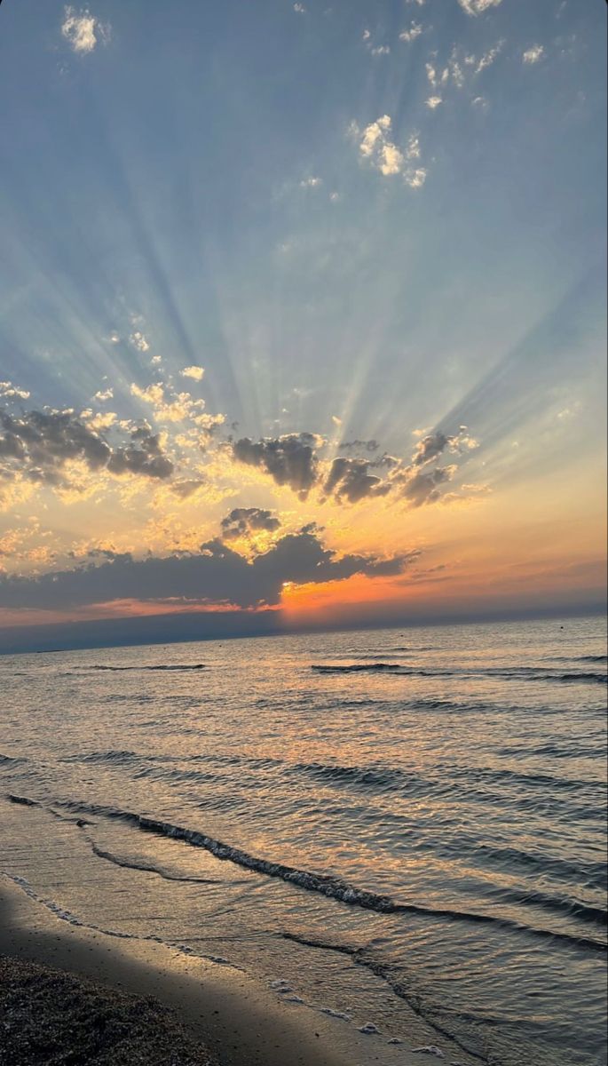 the sun is setting over the ocean with clouds in the sky and waves on the beach