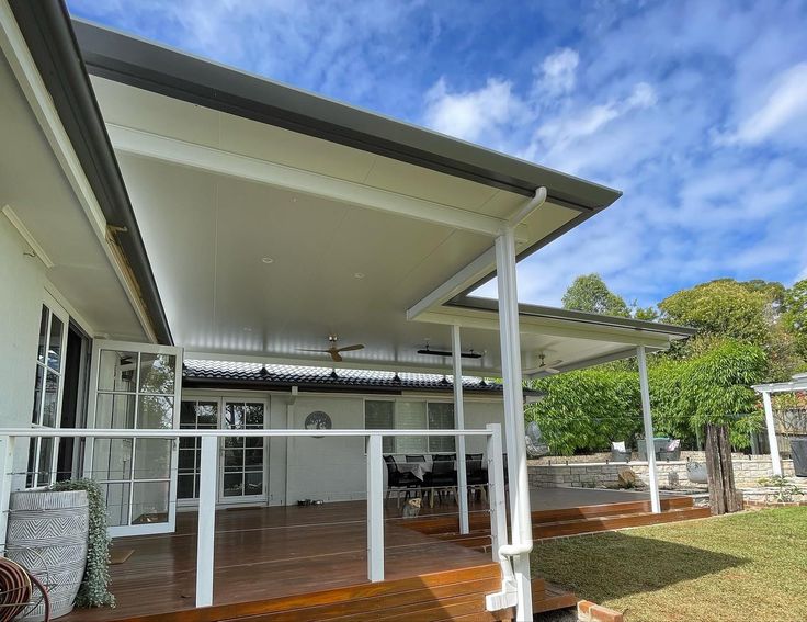 a white house with wooden floors and a covered patio area next to it on a sunny day