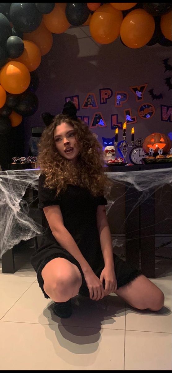 a young woman sitting on the floor in front of balloons and spider webs with her legs crossed