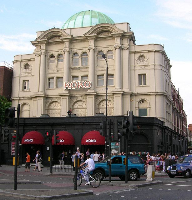 people crossing the street in front of a large building with a green dome on top