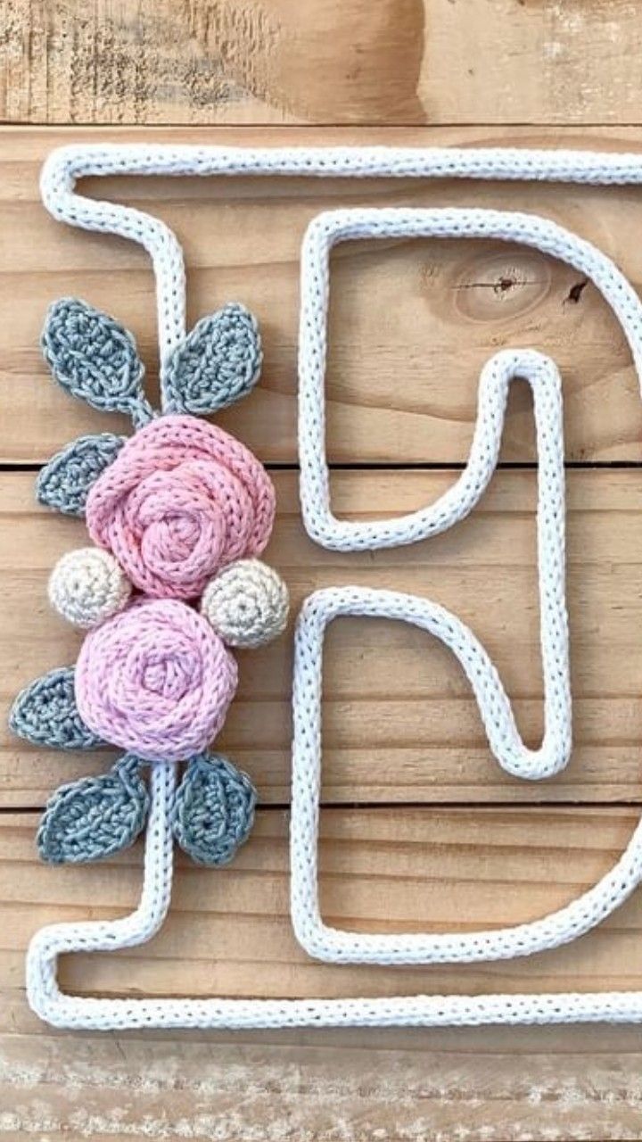 a crocheted letter with flowers and leaves is shown in the shape of a flower