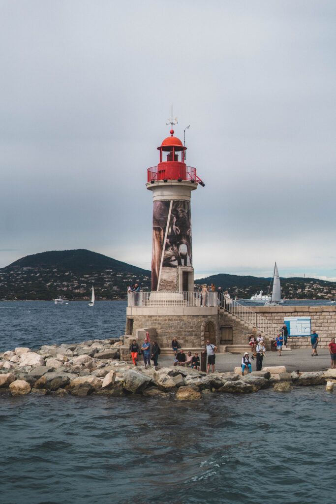 people are standing on the rocks by the water near a light house with a red top