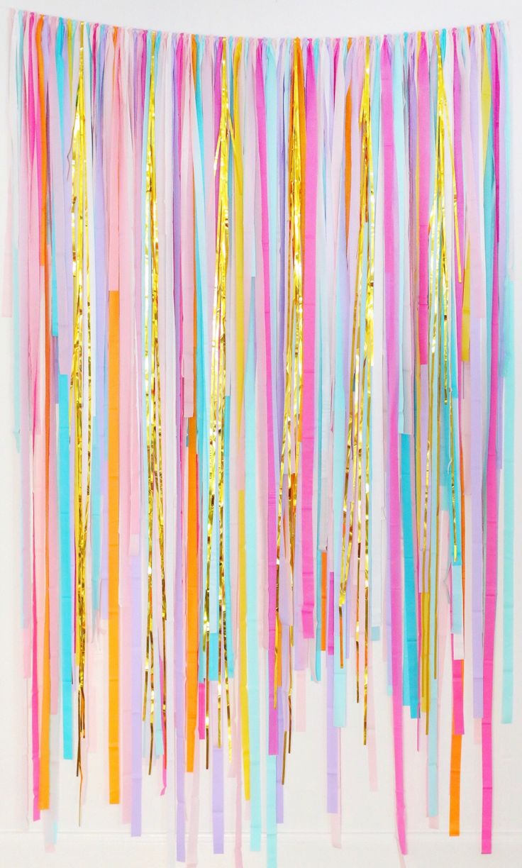 colorful streamers hanging from the ceiling in front of a white wall with pink, yellow and