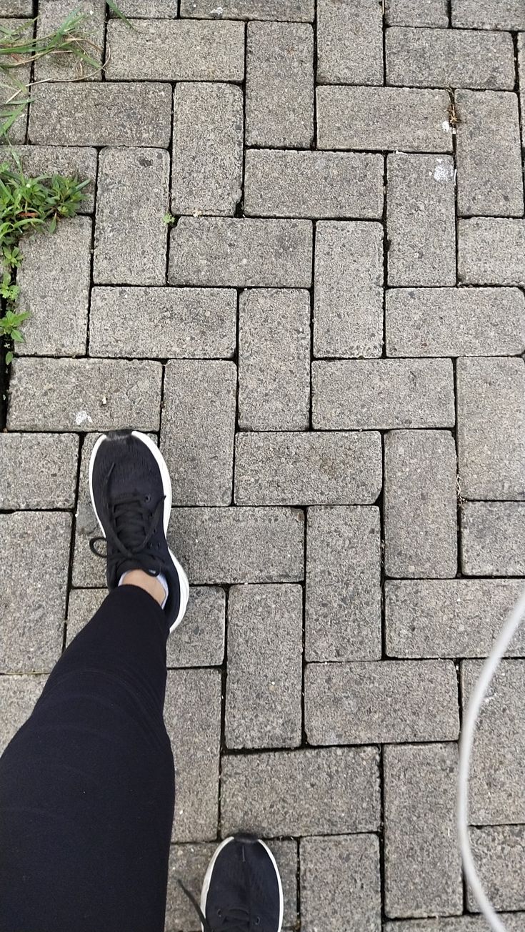 a person standing on top of a brick road next to a green plant and an electric cord