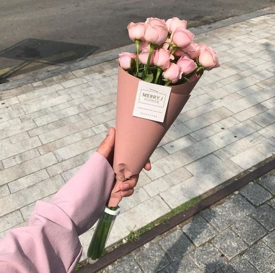 a person holding a bouquet of pink roses on the side of a street in front of a brick sidewalk