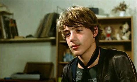 a young man wearing a leather jacket and looking off to the side in front of a bookshelf