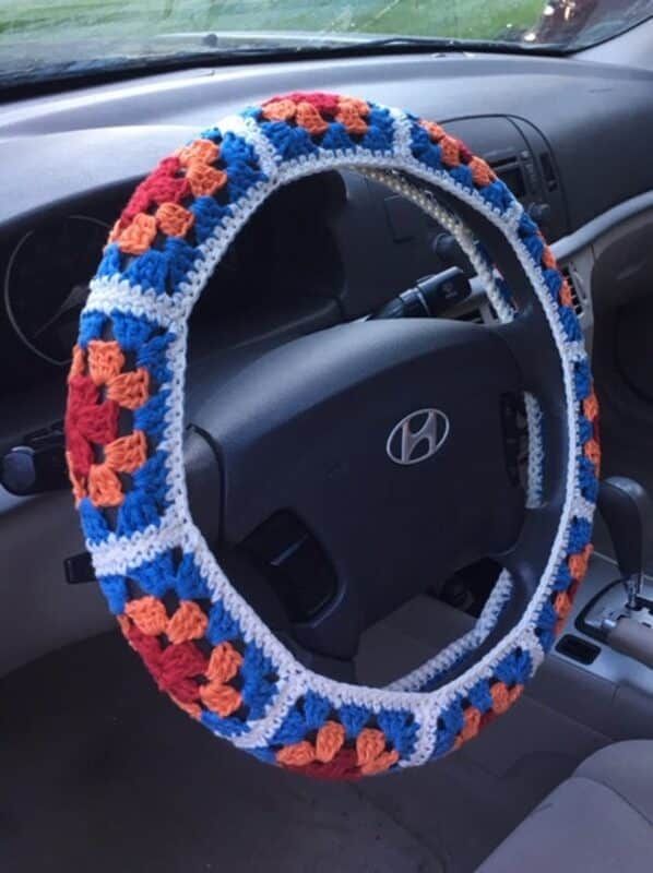 the steering wheel cover is crocheted with an orange, white and blue pattern