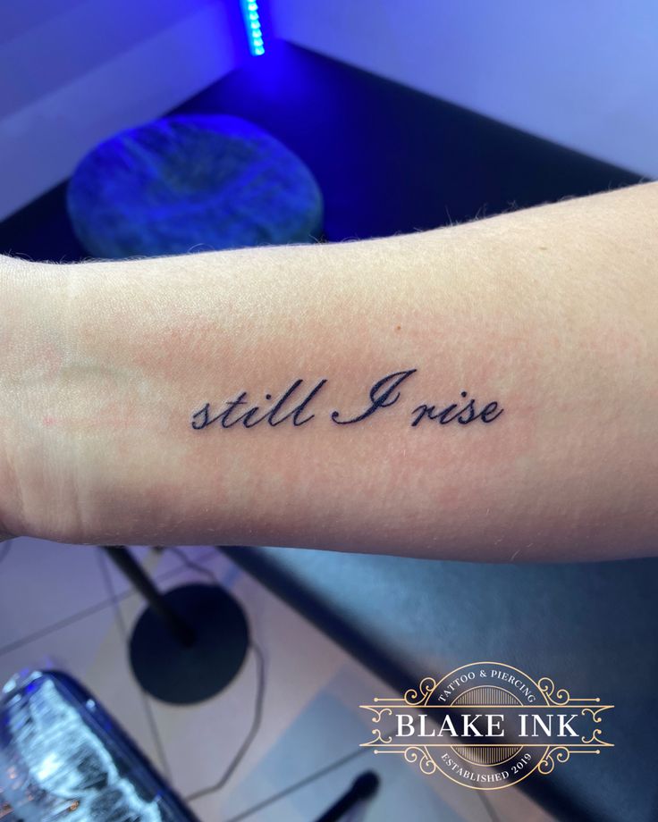 a woman's arm with the words still i rise on it in cursive font