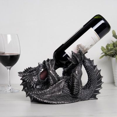 a wine bottle holder with a dragon design on it and a glass of wine in the background