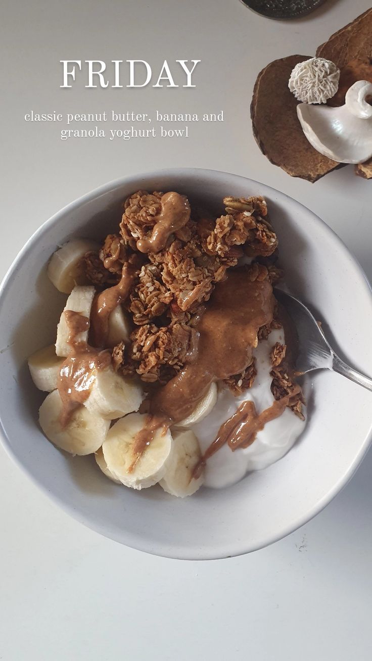 a white bowl filled with bananas and granola on top of a table next to a spoon