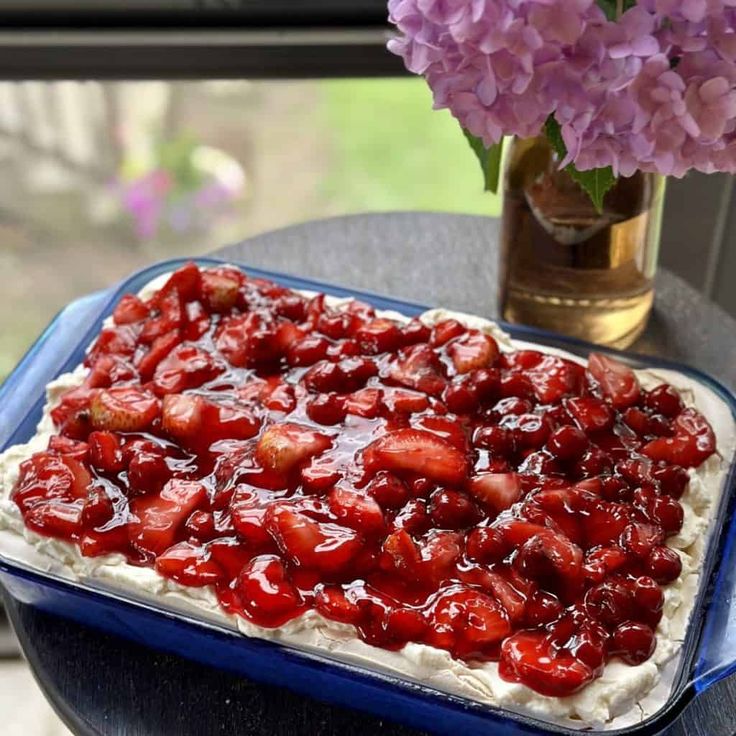 a cake with strawberries on it sitting on a table next to a vase filled with purple flowers