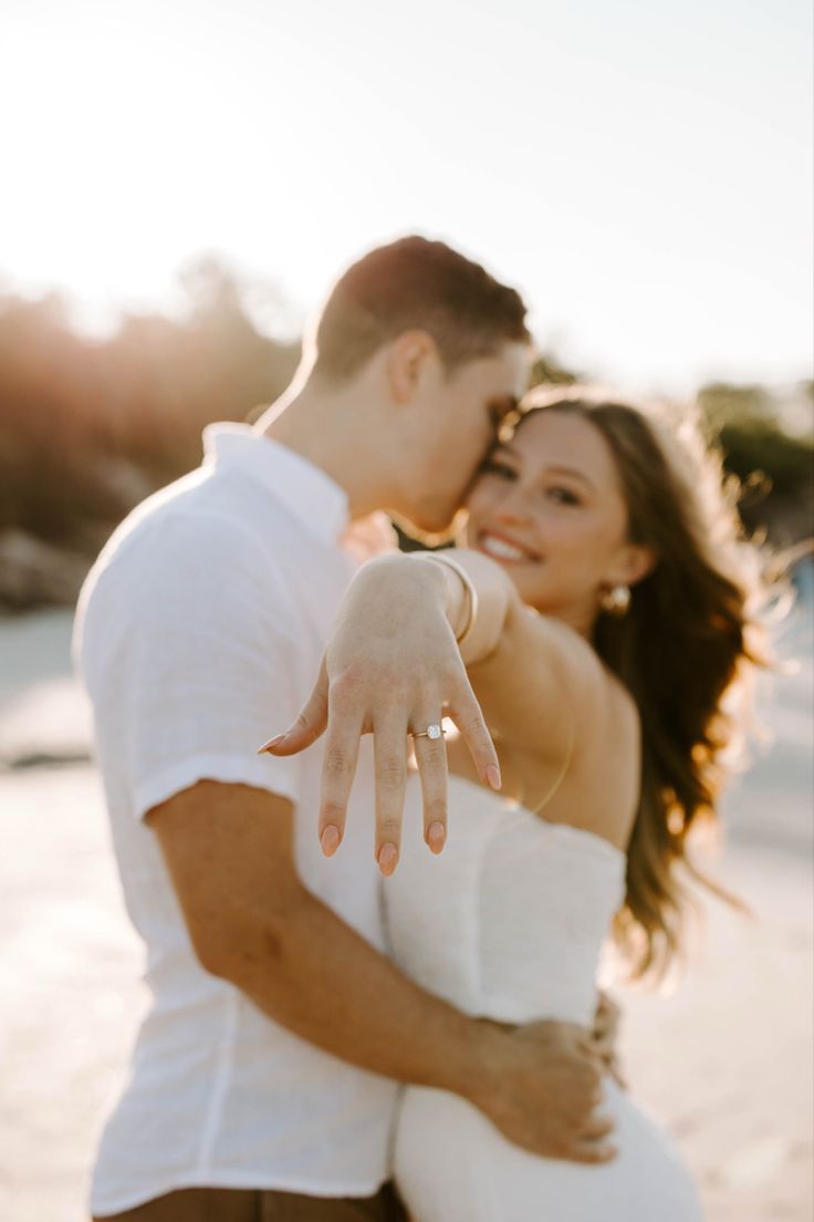 a man and woman standing next to each other in front of the ocean with their arms around each other