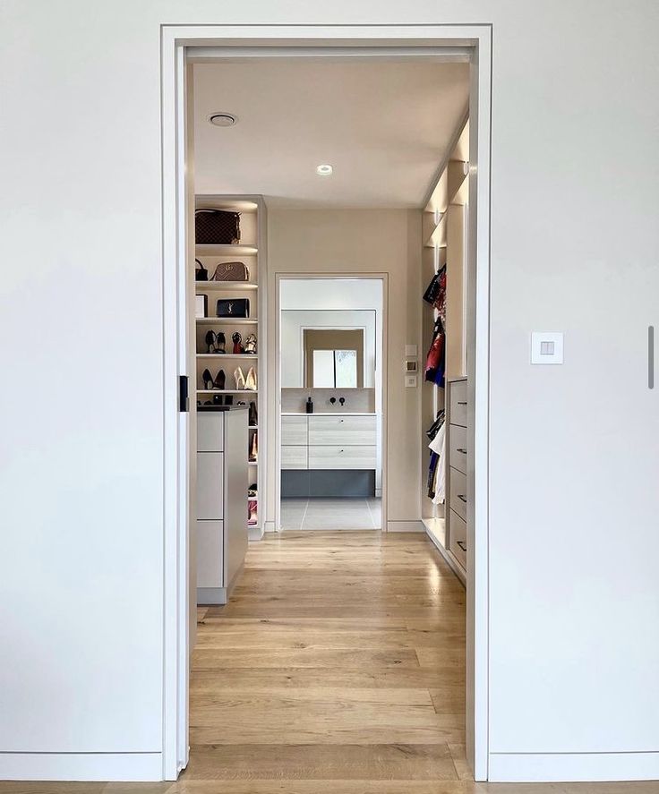 an open door leading to a walk in closet with white walls and wooden flooring