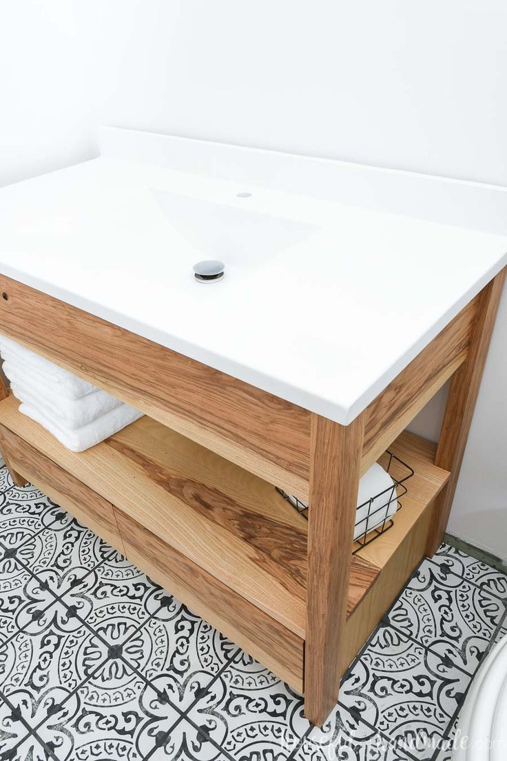 a bathroom vanity with white counter top and wooden drawers on the bottom, next to a black and white tile floor