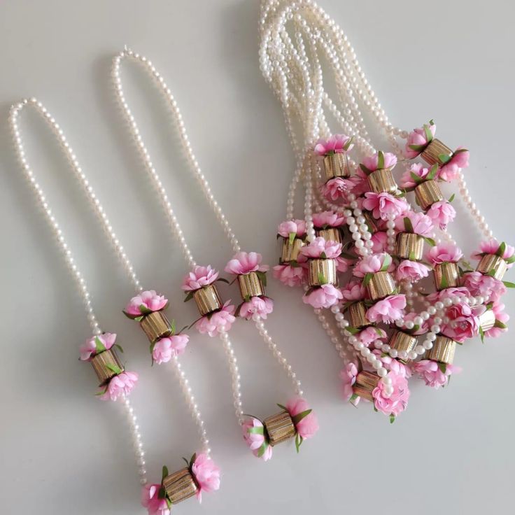 pink flowers and pearls are attached to necklaces on a white surface with two strings