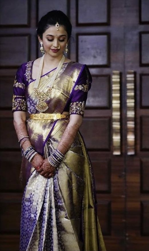 a woman standing in front of a wooden door wearing a purple and gold sari