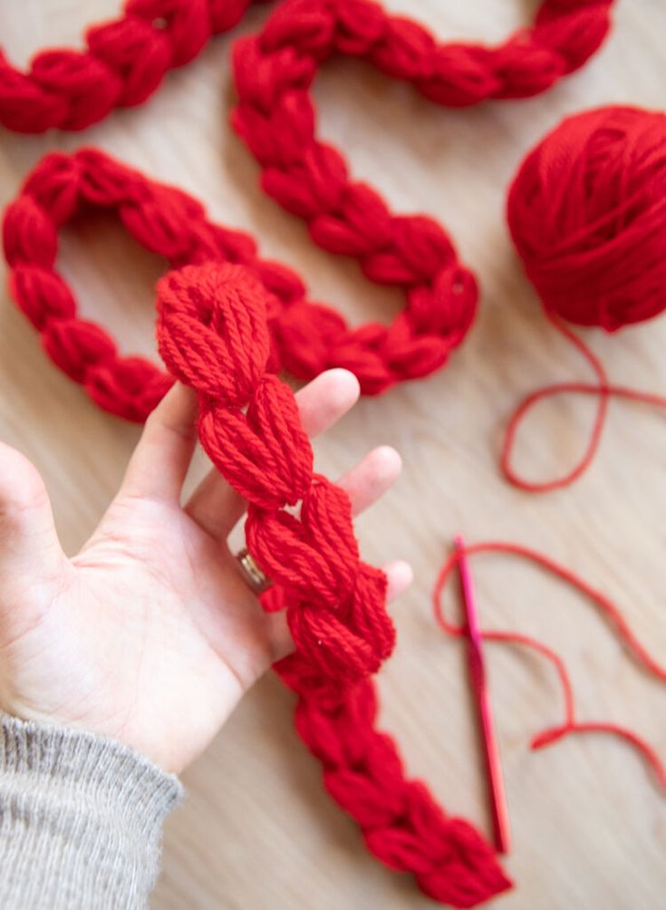 a hand holding a red rope with yarn next to it on top of a table