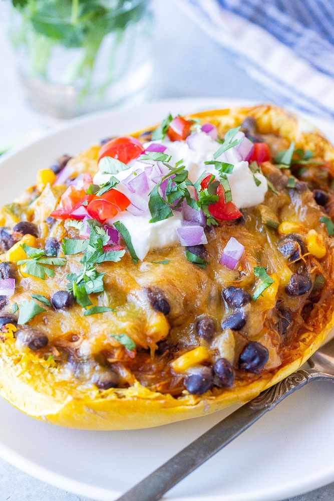 a white plate topped with an enchilada covered in cheese and toppings